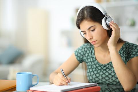 Female autistic student with noise-cancelling earphones writing in a notepad