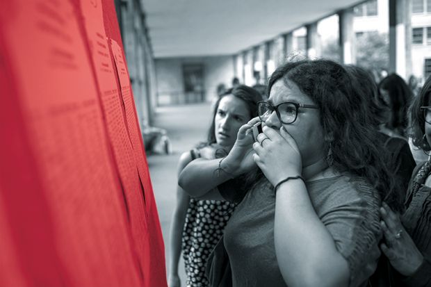 A woman on a mobile phone looks anxiously at a set of results on a board